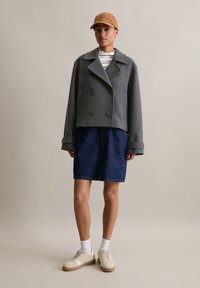 Grijze, cropped, dubbelzijdige wolmix jasje met grote knopen, gecombineerd met een denimrok en beige sneakers. Zacht, textuurhoudend materiaal.