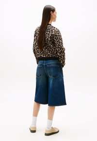 Leopardmønstret genser med ribbestrikket kant, sammen med blå denim culotter. Modellen har på seg beige joggesko og hvite sokker, håret henger rett ned.