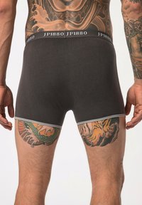 Bóxer negro con una cinturilla gris que presenta el logo "JP1880". La tela es suave, con tatuajes visibles en los muslos.