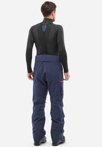 Pantalons de neige bleu marine avec taille réglable, poches zippées et jambes inférieures renforcées. Couche de base noire avec motif géométrique.