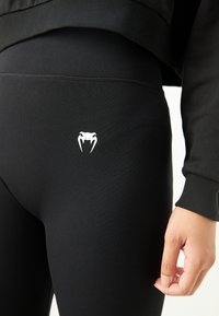 Sorte leggings med ribbet tekstur, med et hvitt slange-logo på låret og elastisk midje for en tettsittende design.