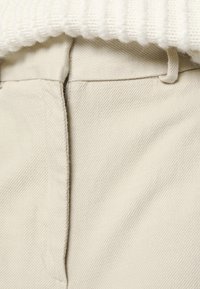 Beige katoenen broek met een gestructureerd oppervlak, voorzien van een voor sluiting en tailleband lussen, gecombineerd met een geribbelde witte stof erboven.