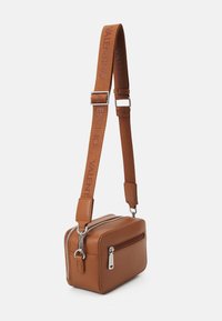 Borsa a tracolla in pelle marrone con forma rettangolare, due compartimenti con zip e una tracolla in tessuto con logo. Design pulito, senza pattern.