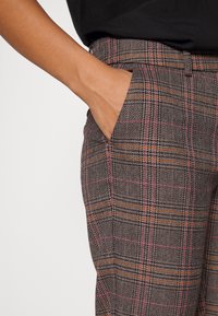 Spodnie w fakturowany, w kratę wzór, z szarymi, różowymi i pomarańczowymi liniami. Widoczna boczna kieszeń, dopasowany krój z wysokim stanem.