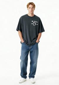 T-shirt oversize noir avec un texte graphique blanc "Mi Amor" et un cœur, associé à un jean bleu ample et des baskets blanches à tige basse.