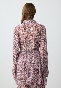 Vestito camicia in tessuto trasparente con stampa leopardata, vita con cintura, maniche lunghe e colletto, caratterizzato da un design morbido e fluido con toni di rosa chiaro.