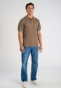 Beige strukturerad pikétröja med korta ärmar och knäppt krage, matchad med blå raka jeans och vita sneakers.