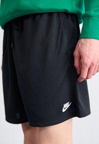 Black Nike athletic shorts with a mesh texture, elastic waistband, and drawstring. Features a white Nike logo on the lower left side.