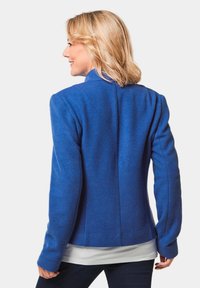 Blaue Fleecejacke mit tailliertem Schnitt, strukturierten Schultern und langen Ärmeln, mit einer glatten Textur und ohne sichtbare Hardware.