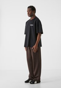 Sort oversized t-shirt med korte ærmer, med hvid logo-tekst. Stylet med løse brune bukser og sorte sko med grå detaljer.