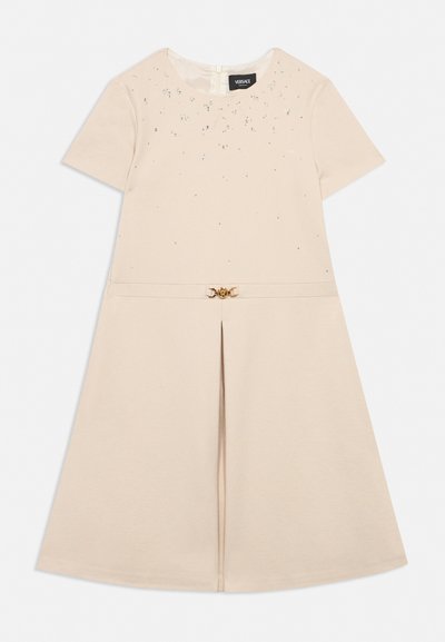 Cream short-sleeve dress with round neck, decorative rhinestones on upper front, pleated skirt, and a gold Medusa belt buckle.