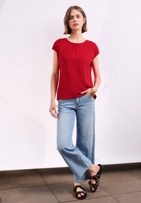 Haut rouge à manches courtes avec un col rond, associé à un jean large bleu clair et des sandales noires avec un motif léopard.