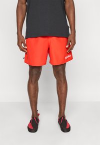 Κόκκινα μαγιό ταχείας στεγνώσεως από ελαφρύ ύφασμα, με ελαστική μέση και λεπτομέρεια λογότυπου. Συνδυάζονται με μαύρα και κόκκινα αναρριχητικά πα πούτσια.