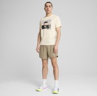 Lys beige t-shirt med grafisktryk, parret med khaki shorts. Modellen bærer hvide sneakers med gule detaljer og hvide ankelsokker.