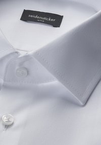 Biała koszula z ostrym kołnierzykiem, o gładkiej fakturze tkaniny. Posiada pojedynczy guzik przy kołnierzyku oraz czarną metkę z białym napisem.