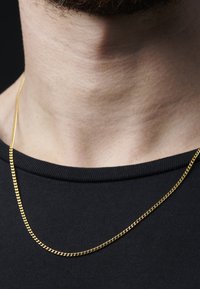 Gullkjede med tvunnet design, liggende på en svart crew-neck skjorte; glatt tekstur, blank overflate og ensartet farge.