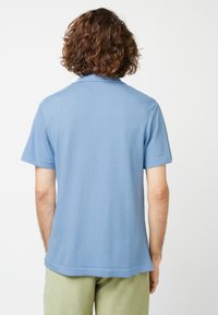 Helles blaues Poloshirt mit kurzen Ärmeln und weicher Textur, mit Kragen und hochgerollten Ärmeln, kombiniert mit grünen Hosen.