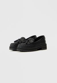 Mustad mustriga nahast loafers, kus on tõmblukudetail ja paks kummitald ning ümar varvas, näidates elegantset disaini ja tekstureeritud viimistlust.