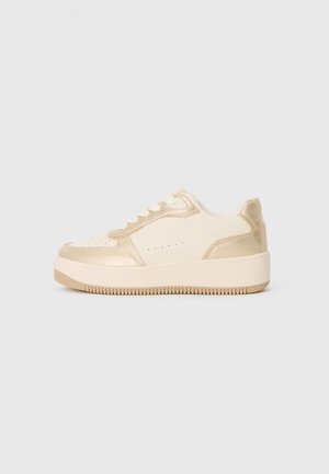 Low-top sneaker in cream and metallic gold with thick sole and white laces, shown in side profile on a plain background.