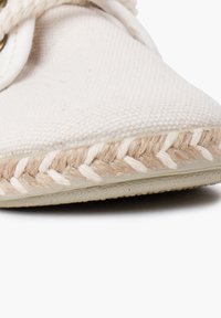 Scarpa slip-on in tela beige con tomaia texturizzata, bordo in juta intrecciata e suola in gomma flessibile. Presenta un design con punta arrotondata.