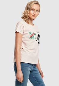 Lyserød bomulds T-shirt med korte ærmer, der har grøn tekst "FØLG DINE DRØMME" og en sort grafik af en figur med et rødt "AFLYST" stempel.