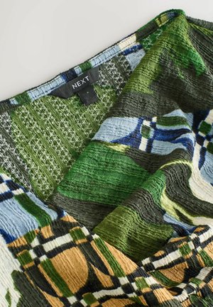 Wielokolorowa tkanina o teksturowanej powierzchni, z zielonymi, niebieskimi i brązowymi łatami w kratkę. Etykieta z napisem "NEXT".