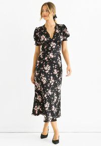 Black floral dress with pink flowers, short puff sleeves, V-neckline, lace trim, and a flowing skirt, paired with black pumps.