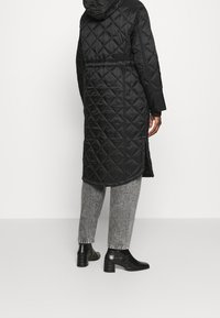 Abrigo acolchado negro con capucha, con cintura ajustada y mangas largas. Combinado con pantalones gris con estampado y botines negros de tacón.