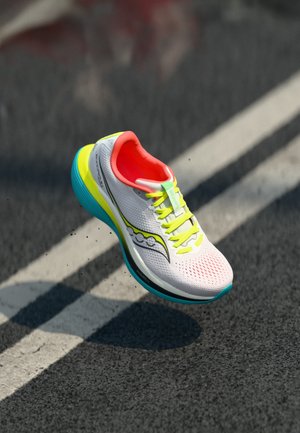 Hardloopschoen met een witte mesh bovenkant, feloranje voering, groene veters en een blauwe en gele zool met een gestructureerd patroon.