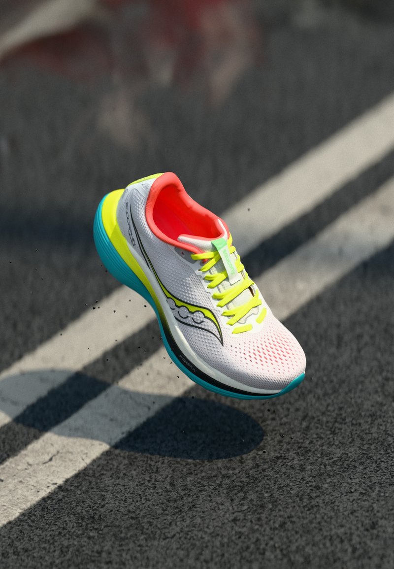 Des chaussures de course avec une tige en maille blanche, un intérieur orange vif, des lacets verts et une semelle bleue et jaune présentant un motif texturé.