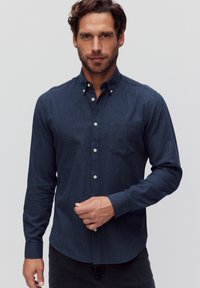 Donkerblauwe overhemd met kraag, lange mouwen en één borstzak, gemaakt van een gestructureerde stof, met witte knopen.