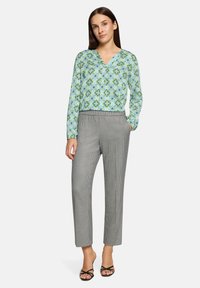 Bluzka w kwiatowy wzór w kolorach zielonym, niebieskim i białym; do tego szare spodnie w kratę; modelka ma na sobie czarne sandały z paskami.