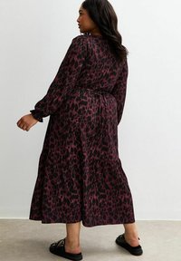 Robe longue avec une base sombre ornée d'un imprimé léopard bordeaux, des manches longues, une taille cintrée et une jupe à volants, fabriquée en tissu léger.