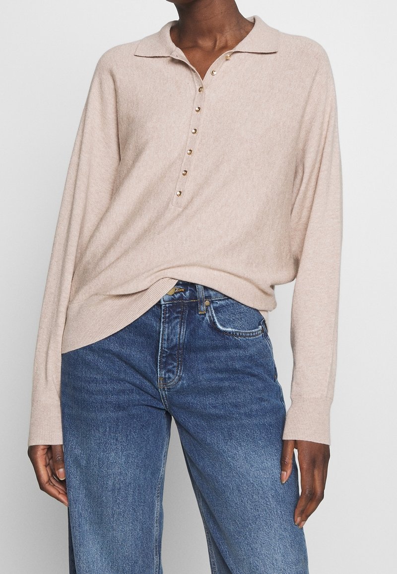 Beige stickad tröja med polokrage, med knappslå och långa ärmar. Matchad med blå denimjeans. Mjuk textur.