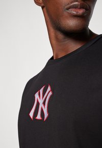 Black cotton t-shirt featuring a prominent embroidered white and red New York Yankees logo on the chest, with a crew neckline.