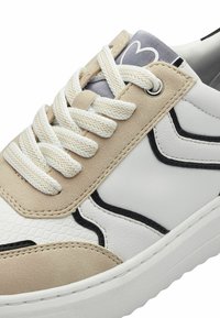 Beige és fehér sneaker fűzős dizájnnal, texturált bőrrel, sima részletekkel, fekete körvonalakkal és párnázott talppal.