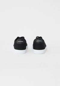 Sneakers neri in tela con suole in gomma bianca. Presentano un design a low-top e un logo sulla parte posteriore. I lacci sono neri, con una texture minima.
