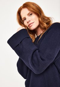 Marineblau strukturierter Pullover mit breiten, gerippten Bündchen; hat ein lockeres Design und einen runden Ausschnitt. Weiches Strickmaterial mit Musterelementen.