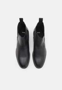 Botas de tobillo de cuero negro con acabado suave, paneles laterales elásticos y lengüetas. Punta redonda y diseño minimalista para un uso versátil.