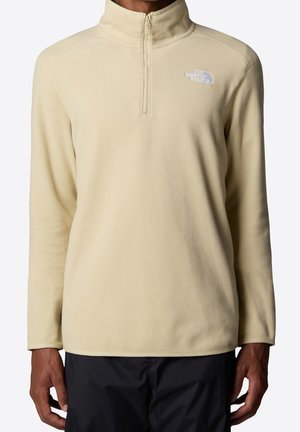Beige fleece trui met lange mouwen en een kwart rits, met het logo van The North Face op de linkerborst, gedragen met een zwarte broek.