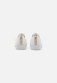 Weiße Sneakers mit glatter Oberfläche, ausgestattet mit einem strukturierten beigen Fersenband und dezenten Branding-Elementen. Gummisohlen und minimalistische Designdetails.
