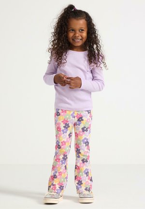 Top a maniche lunghe viola a coste abbinato a pantaloni in corda a fiori pastello svasati. Scarpe in tela completano l'outfit.