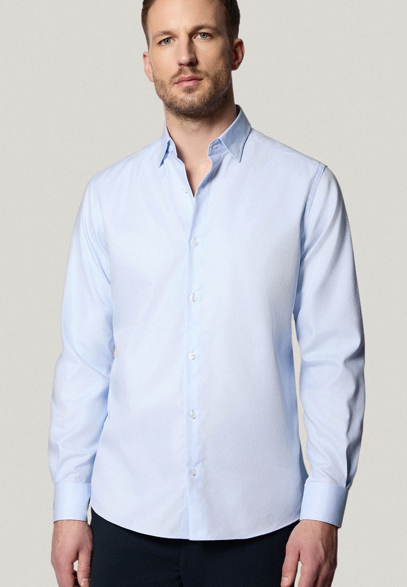 Jasnoniebieska koszula zapinana na guziki z klasycznym kołnierzykiem, długimi rękawami i gładką fakturą. Posiada białe guziki i dopasowany krój.