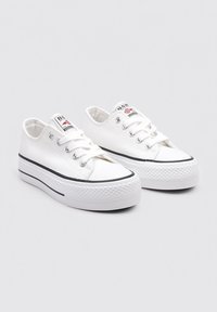 Baskets en toile blanches avec un bout arrondi, semelle en caoutchouc noir et parois latérales texturées. Comprend des œillets et des lacets ; logo subtil sur la languette.