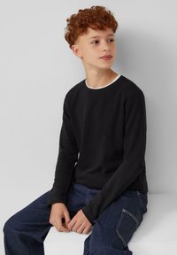 Zwarte langemouwen shirt met een witte halslijn, gemaakt van een zacht materiaal, gedragen met donkerblauwe denim broek, met een relaxte pasvorm.