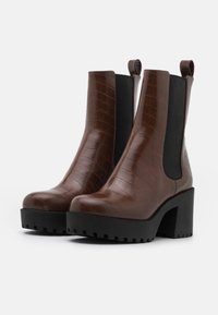 Botas de tobillo de imitación de cocodrilo marrón con paneles laterales elásticos negros y tacones de plataforma negros gruesos. Superficie texturada y diseño de punta redondeada.