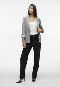 Blazer gris avec les manches retroussées, haut blanc et jeans droits noirs. Talons aiguilles noirs. Lignes simples et épurées dans des couleurs classiques.