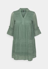 Rochie verde deschis din dantelă, cu un guler înalt, mâneci trei sferturi și modele detaliate pe toată suprafața. Are accente cu mâneci evazate.