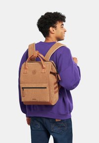 Zaino in velluto a coste marrone con accenti in pelle beige, motivo trapuntato, spallacci robusti e una tasca frontale con zip nera.