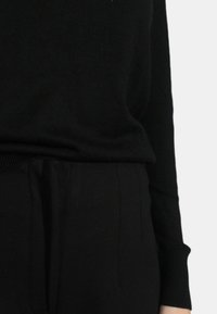Maglione nero a maglia con scollatura rotonda e maniche lunghe, abbinato a pantaloni neri a vita alta con pieghe e una texture liscia.
